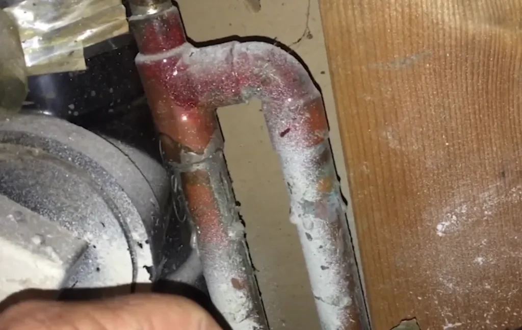Copper water lines coated in heavy corrosion and mineral deposits beneath a home, the kind of hidden damage that drives up slab leak repair pricing