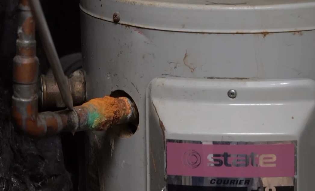 Heavily corroded copper pipe connection at a water heater, one of the common slab leak signs and repair cost factors homeowners should know