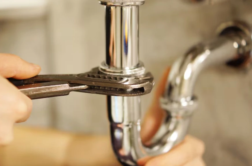 Plumber tightening a chrome drain pipe with a wrench during an urgent leak repair, the kind of fix an emergency plumber Fort Worth residents call for after hours