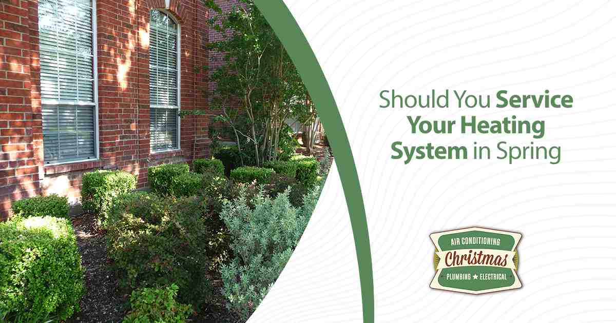 Brick house exterior with shrubs promoting heating system service in spring.