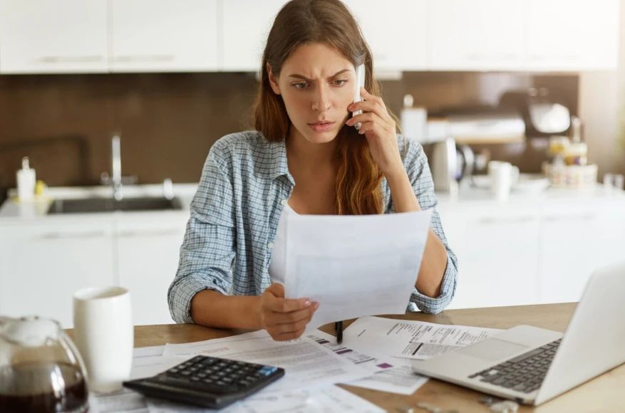 Woman reviewing a high summer electric bill at her kitchen table while researching how to lower electric bill in summer DFW