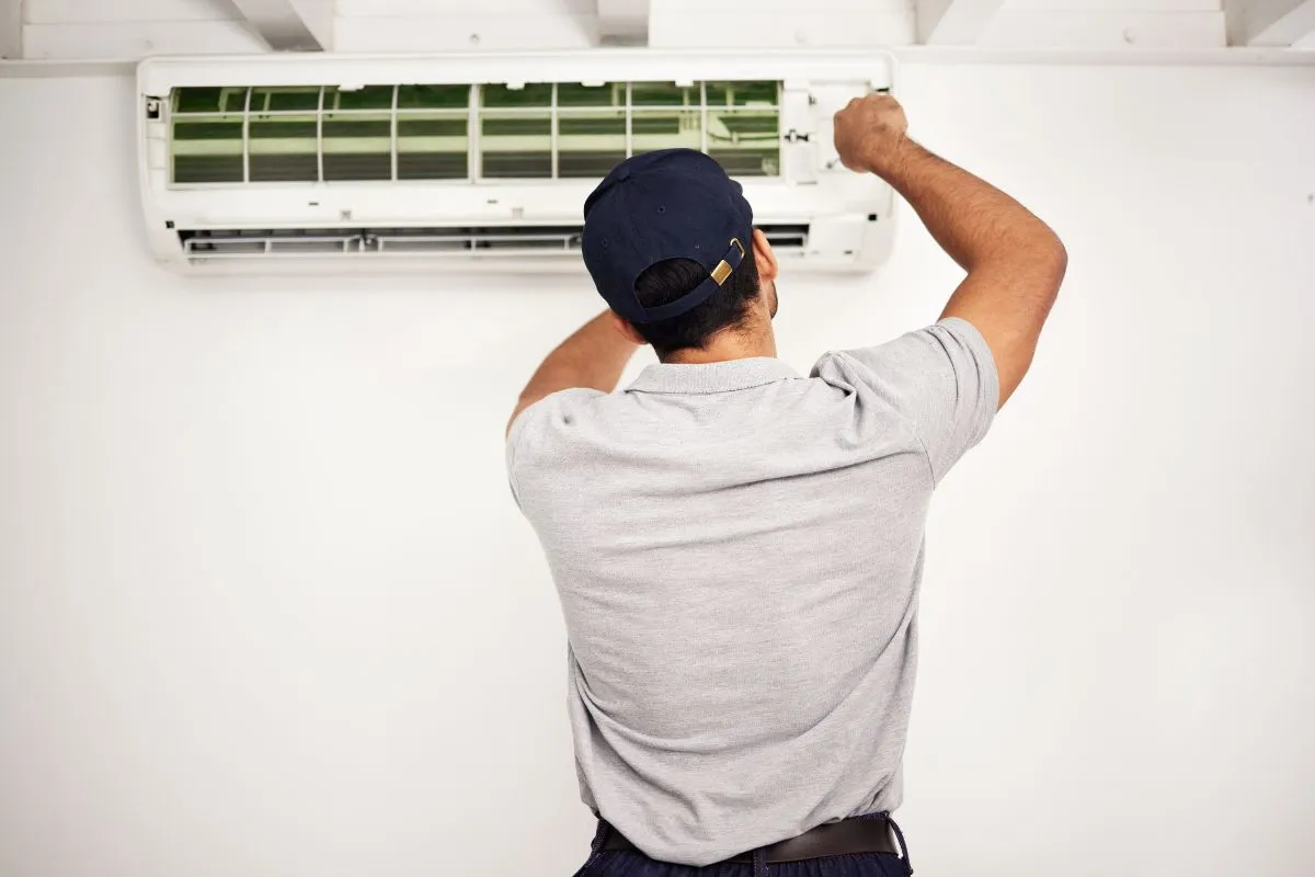 Best time to replace AC in Texas as a technician services a wall-mounted air conditioner