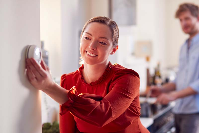 Woman adjusting thermostat, turning up the heat in her home.